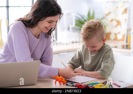 Work from home and family education, Mom and son using remote access technology for learning and work, woman works on laptop, child writes in textbook Stock Photo