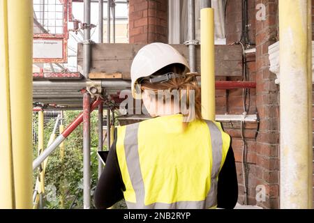 Female chartered civil engineer working in a construction site building, taking notes on her tablet, condition inspection survey, hard hat and yellow Stock Photo