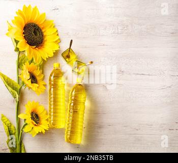 Plastic bottles with sunflower oil, fresh yellow sunflowers.Flat top view copy space.Composition with sunflower oil on white wooden table. Stock Photo