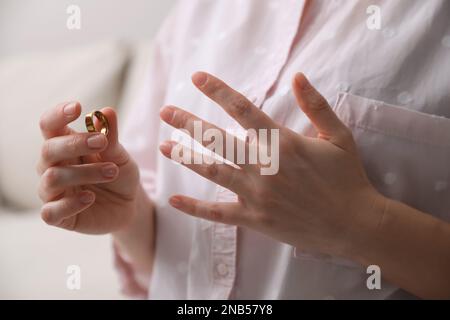 Woman taking off wedding ring indoors, closeup. Divorce concept Stock Photo