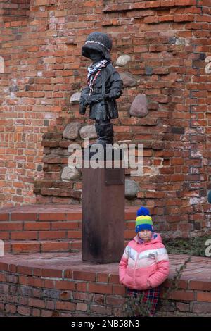 A child standing by the Mały Powstaniec - The Little Insurrectionist-  statue honours the children who fought Nazis in Poland. Warsaw, Poland Stock Photo