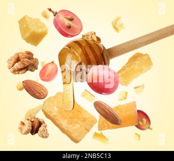Pieces of delicious parmesan, nuts, grapes and honey falling on yellow background Stock Photo