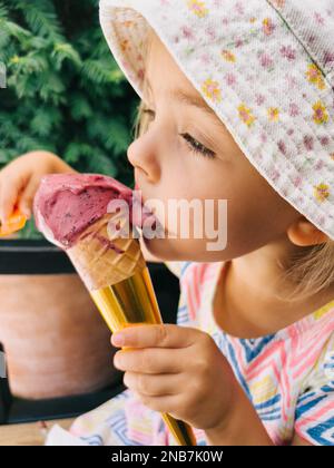 Little girl licks a popsicle in a cone, holding it in her hand Stock Photo