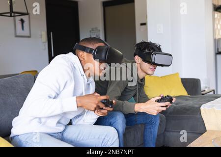 Image of diverse male teenage friends with vr glasses playing video games at home. Hanging out with friends and spending quality time together concept Stock Photo