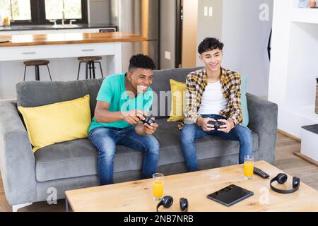 Happy diverse teenager male friends playing video games at home. Hanging out with friends and spending quality time together concept. Stock Photo