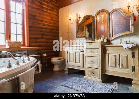 Bleached and distressed pinewood cabinets, antique wall-mounted folding mirror, white porcelain toilet and bathtub in main bathroom on upstairs floor. Stock Photo
