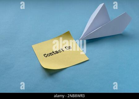 Contact us concept written on yellow memo note with paper plane on blue background. Stock Photo