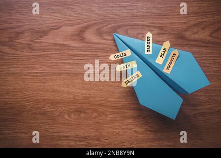 Blue paper plane with sticky notes written with Goals, Aim , Desire, Target , Plan and Objective with copy space on wooden background. Stock Photo