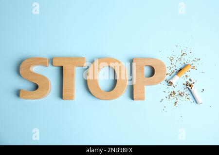 Broken cigarette near word Stop made with wooden letters on light blue background, flat lay. Quitting smoking concept Stock Photo