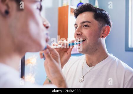 Two gay men brushing their teeth in the bathroom looking at each other. Daily life of a homosexual couple Stock Photo