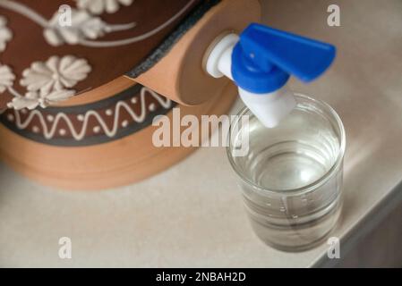 A glass of water from traditional water dispenser called Labu Sayong ...