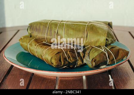 Wrapped Hallaca or Tamale over a rustic table and a blue dish, Mexican and Venezuelan traditional food Stock Photo