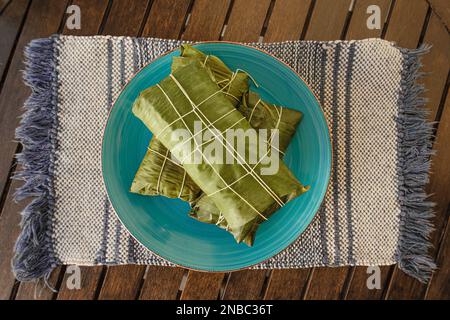 Wrapped Hallaca or Tamale over a rustic table and a blue dish, Mexican and Venezuelan traditional food Stock Photo