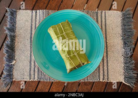 Wrapped Hallaca or Tamale over a rustic table and a blue dish, Mexican and Venezuelan traditional food Stock Photo