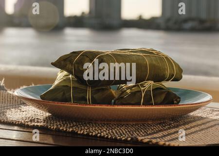 Wrapped Hallaca or Tamale over a rustic table and a blue dish, Mexican and Venezuelan traditional food with a Miami, Florida background Stock Photo