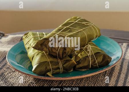 Wrapped Hallaca or Tamale over a rustic table and a blue dish, Mexican and Venezuelan traditional food Stock Photo