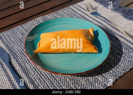 Hallaca or Tamale over a rustic table and a blue dish, Mexican and Venezuelan traditional food Stock Photo