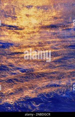 Rippling water sparkles under warm sunset colours, painting the sea with golden and orange tones Stock Photo