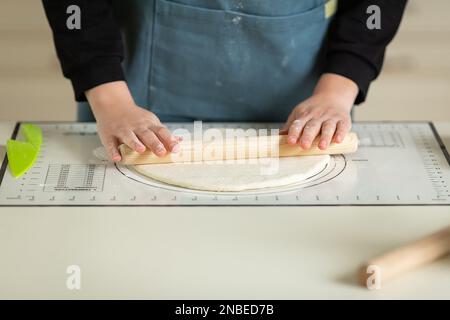 Rolling out the dough with a wooden rolling pin on a silicone baking mat. View of hands and workspace. copy space Stock Photo