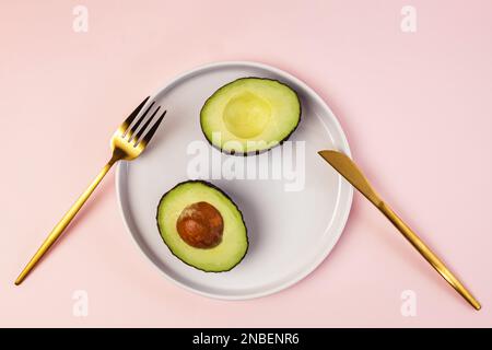 Avocado cut in halves on the plate and golden color flatware, top view Stock Photo