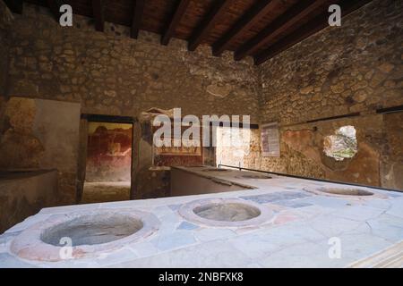 The kitchen with frescos on the wall and canisters in the counter at Casa e Thermopolium di Vetutius Placidus. At Pompeii Archaeological Park near Nap Stock Photo
