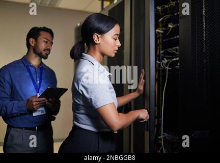 Server room, engineer teamwork and woman opening panel for maintenance or repairs at night. Cybersecurity, programmers and female with man holding Stock Photo