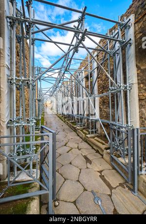 Preservation, restoration work with metal scaffolding being done along a cobblestone street. At Pompeii Archaeological Park near Naples, Italy. Stock Photo
