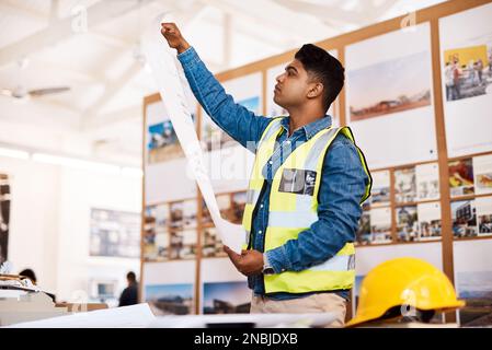 I cant wait to show this to my client. a young architect looking at a blueprint in his office. Stock Photo