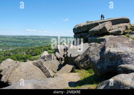 Two people view Wharfedale from the Cow and Calf Rocks, Ilkley Moor, Rombalds Moor, West Yorkshire, UK Stock Photo