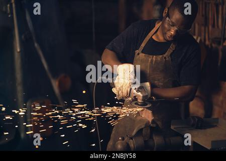 .As in life, the successful forge on. a young man using an angle grinder while working at a foundry. Stock Photo