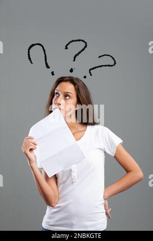 Thin young woman with letter causing her doubts or thoughts, carries a hand at her side and the document in front of her face, the graphic represents Stock Photo