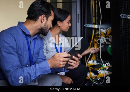 Engineer teamwork, server room and tablet for connection cable, maintenance or software update at night. Cybersecurity wire, programmers or man and Stock Photo