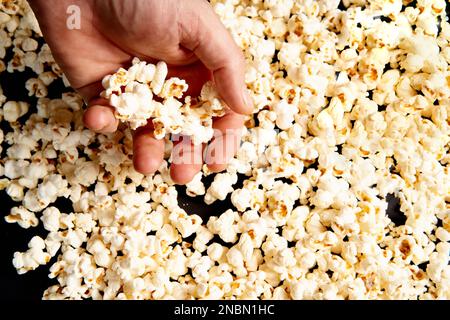 Popcorn in men's hands. Flat lay . Texture or background of scattered crispy popcorn on a black isolated background. Movies, advertising. Stock Photo