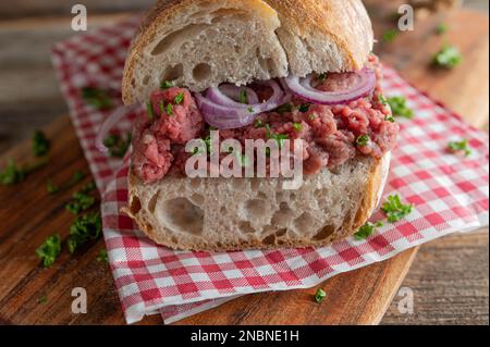 Raw beef sandwich with red onions and parsley on a french baguette. Closeup and front view Stock Photo
