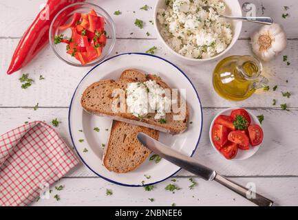 Feta cheese salad with olive oil and herbs served with roasted sourdough bread and vegetables on white background. Flat lay Stock Photo