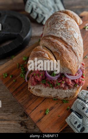 Raw beef sandwich on a rustic baguette bread with red onions and parsley on wooden table Stock Photo