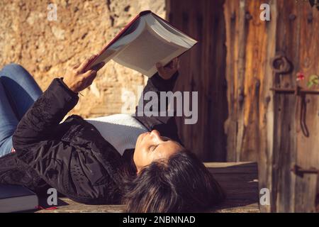 latin woman lying down, reading a book in the garden Stock Photo