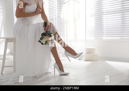 Young bride with bouquet wearing wedding shoes indoors. Space for text Stock Photo