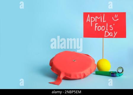 Sign with phrase Happy Fools' Day and clown's accessories on light blue background, space for text Stock Photo