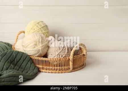 Woolen yarns in basket on white wooden table. Space for text Stock Photo