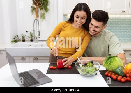Handsome guy helping his pretty girlfriend making dinner at home Stock Photo