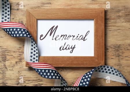 Frame with phrase Memorial Day and ribbon on wooden table, flat lay Stock Photo