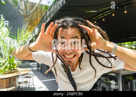 young latino man with dreadlocks of venezuelan ethnicity, he is desperate with his hands on his head and with a funny face, standing in front of a res Stock Photo