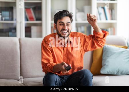 Emotional arab man watching TV at home, gesturing Stock Photo