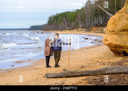 An elderly couple was walking along the seashore on a February day. One day before Valentine's Day, love. Baltic Sea coast, Veczemju cliff. Stock Photo