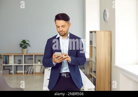 Businessman standing in office and using modern business app on his mobile phone Stock Photo