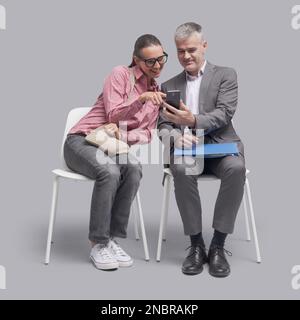 Happy people sitting next to each other and watching videos on a smartphone Stock Photo