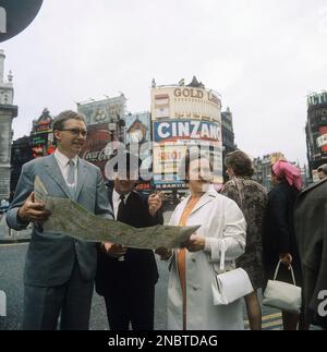 London 1972. A couple seemingly tourists at Piccadilly Circus in London trying to find their way. They are holding a map and a helpful gentleman points them in the right direction. Piccadilly circus is known for being the place where the first traffic lights were installed 3 august 1926. At one time all of the house were covered in advertising signs and neon.  Kristoffersson ref DV7 Stock Photo