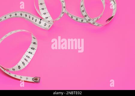 Unfolded white tape measure, White measuring tape isolated on pink background. Close the tailor measuring tape on a pink background. The concept of sp Stock Photo