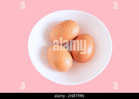 chicken egg, three chicken eggs isolated on white plate background, white plate with chicken eggs on pink background, Creative minimal concept. Stock Photo